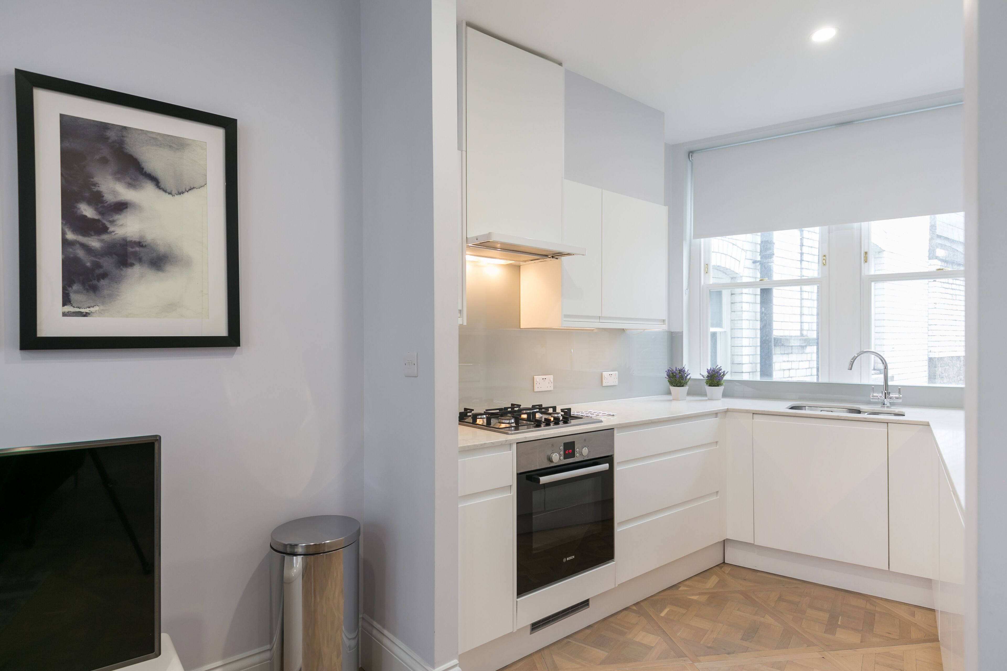 A modern kitchen with white cabinets, a built-in oven, and a window providing natural light.