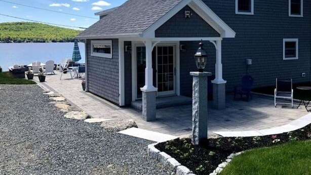 Une maison dotée d’un porche couvert, d’une petite terrasse et d’un pilier en pierre.