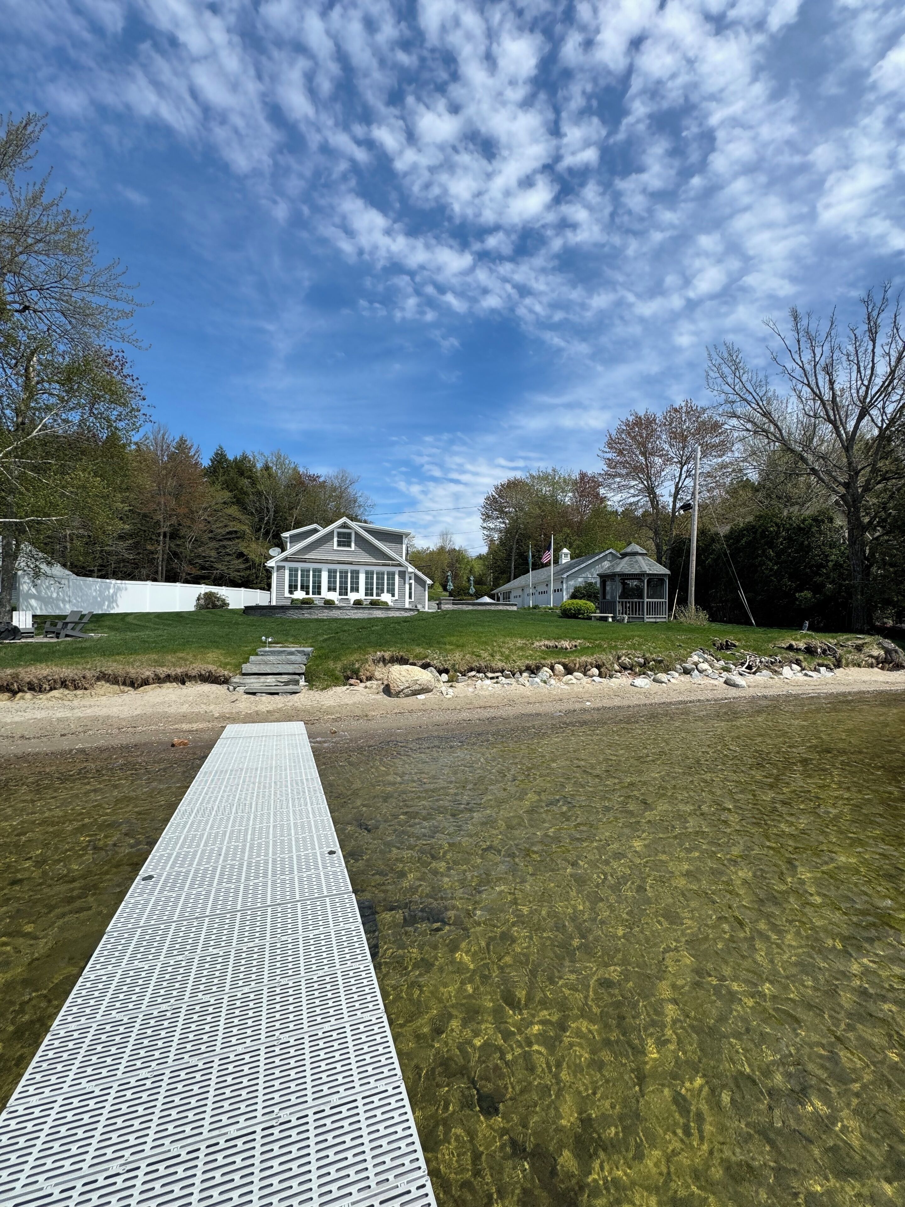 A clear view of a house with a large porch, a grassy area, and a body of water in the foreground.