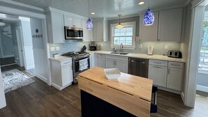 Une cuisine moderne avec des meubles blancs, un plan de travail en bois, des appareils électroménagers en acier inoxydable et des luminaires suspendus.