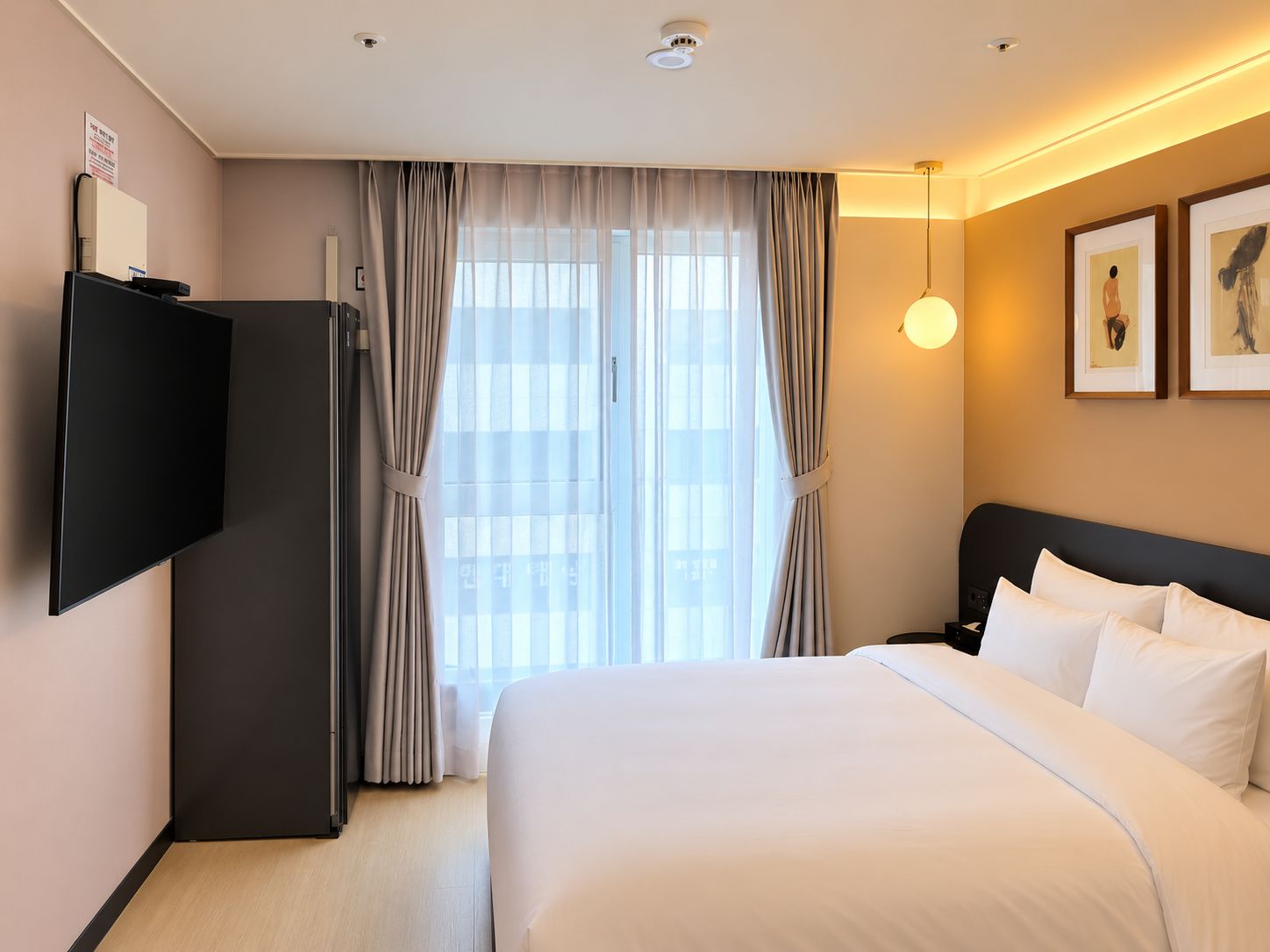 A hotel room with a bed, a flat-screen TV, a desk, and a window with curtains.