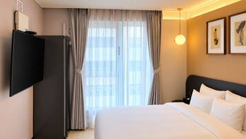 A hotel room with a bed, a flat-screen TV, a desk, and a window with curtains.