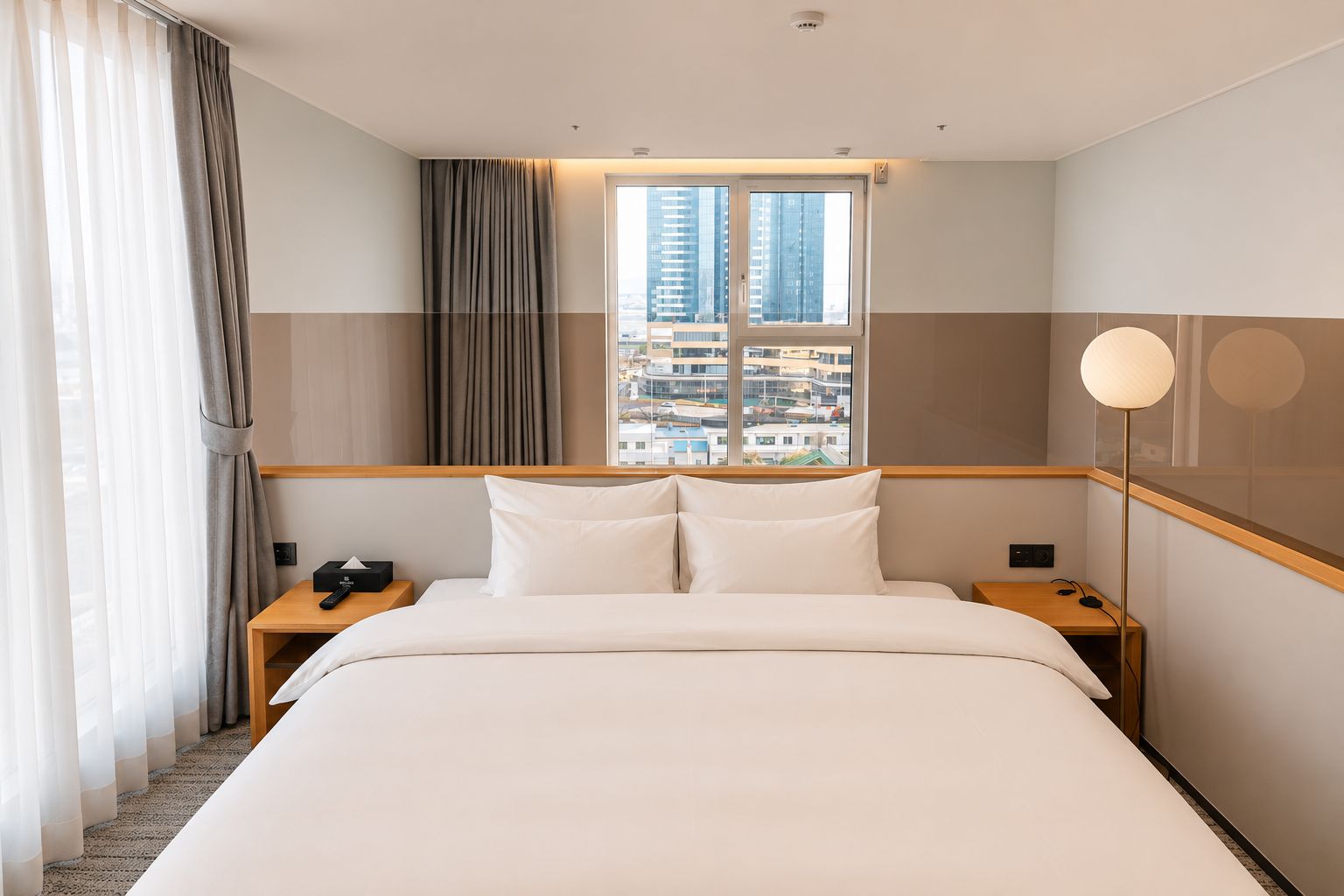 Une chambre d’hôtel avec un grand lit, une table de chevet, une lampe et une fenêtre donnant sur la ville.