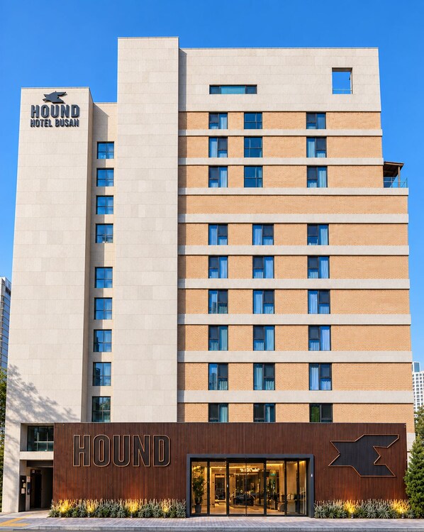 A multi-story hotel with a prominent sign reading 'HOUND HOTEL BUSAN' and a modern facade with a mix of brick and concrete materials.
