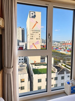 Una habitación con un ventanal grande que da a un paisaje urbano, incluyendo un edificio alto con un letrero de estacionamiento.