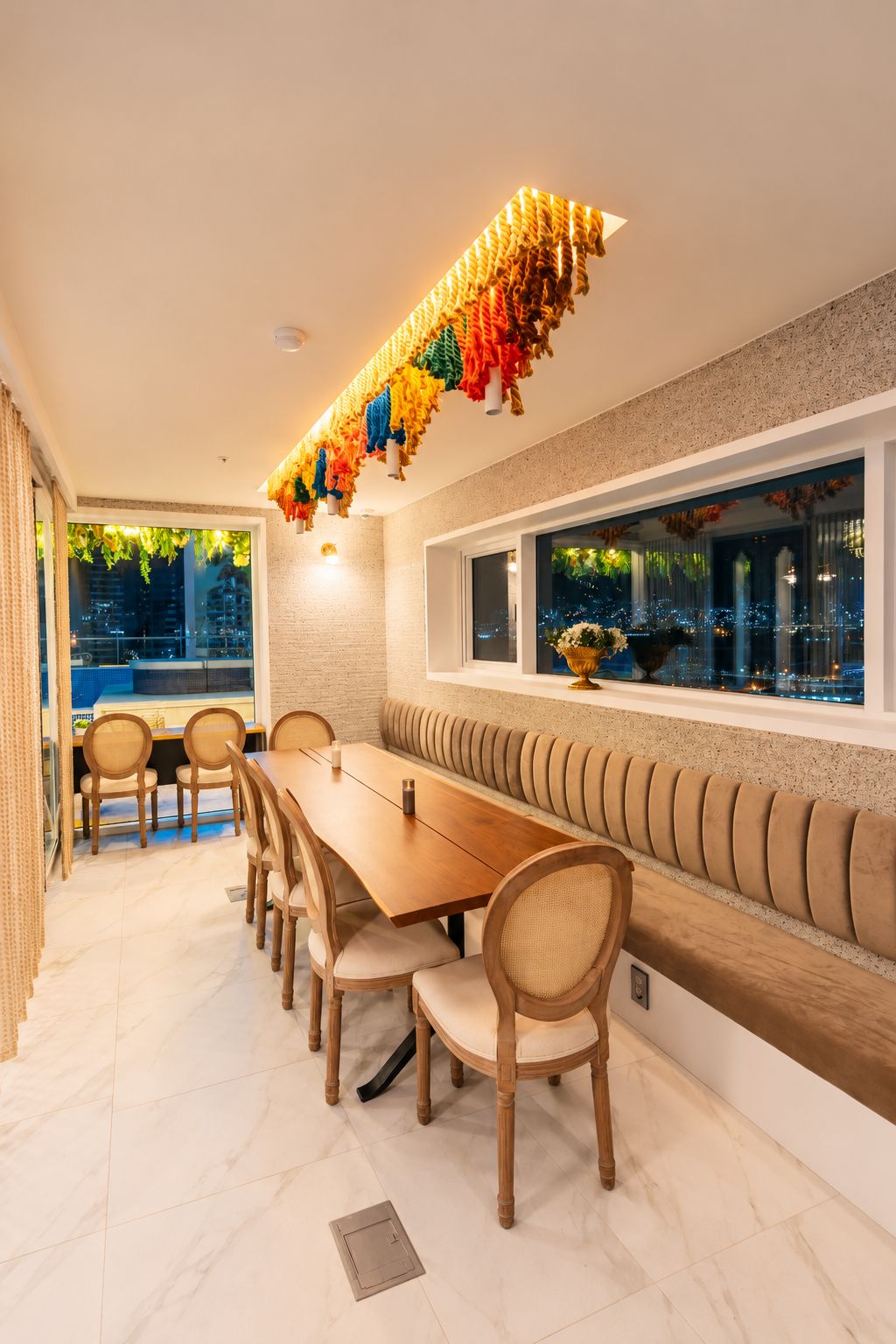 A dining area with a long wooden table, cushioned chairs, and a bench along the wall.