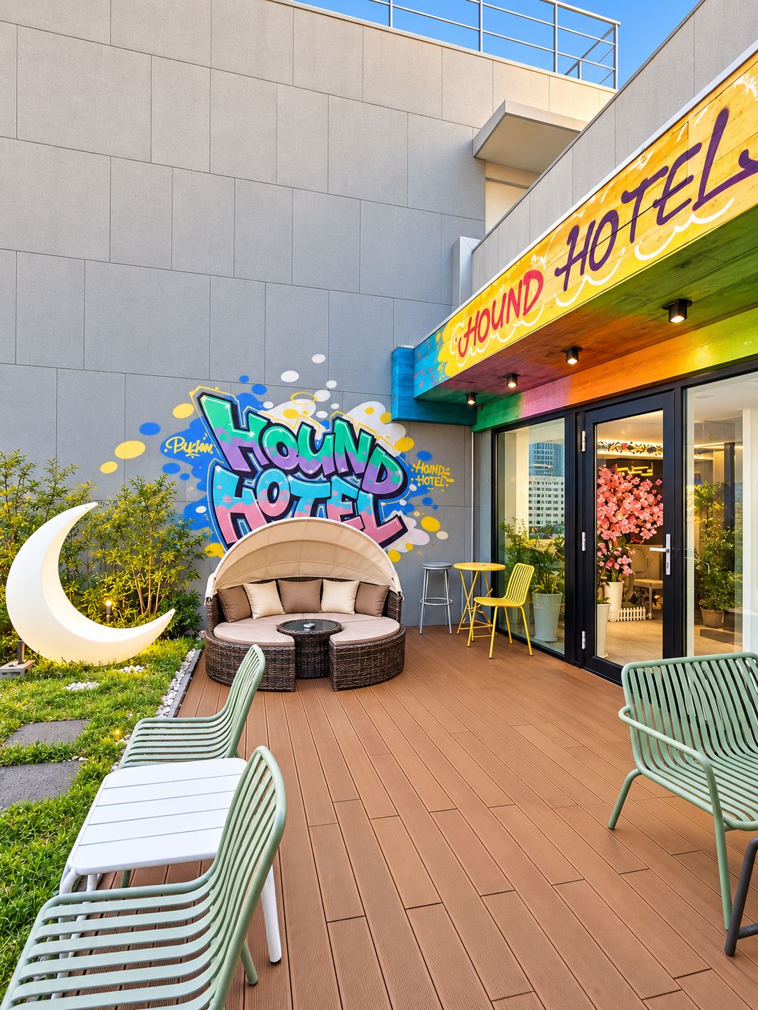 L’extérieur d’un hôtel, avec une enseigne colorée, un espace extérieur aménagé avec des sièges et un élément décoratif lumineux en forme de croissant.