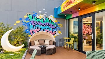 L’extérieur d’un hôtel, avec une enseigne colorée, un espace extérieur aménagé avec des sièges et un élément décoratif lumineux en forme de croissant.