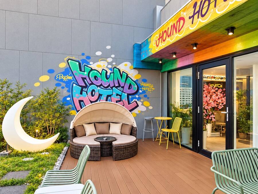 Exterior de hotel con un letrero colorido, zona de estar al aire libre y un elemento decorativo en forma de media luna.