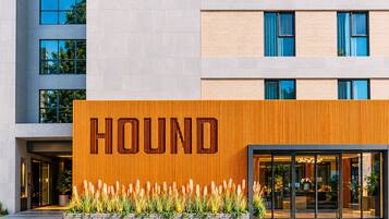 A modern building with a prominent 'HOUND' sign on the facade, featuring a vertical wooden panel design and a landscaped entrance with ornamental grasses.