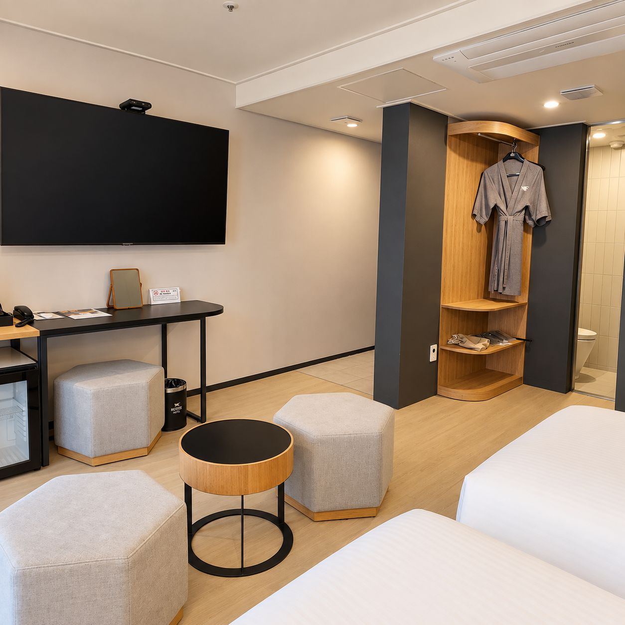 A modern hotel room with a flat-screen TV, a desk with a telephone, and a seating area with ottomans and a round table.