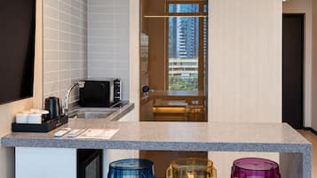 A modern kitchen with a built-in microwave, a coffee machine, and a sink. There are colorful stools and a window with a view of buildings.