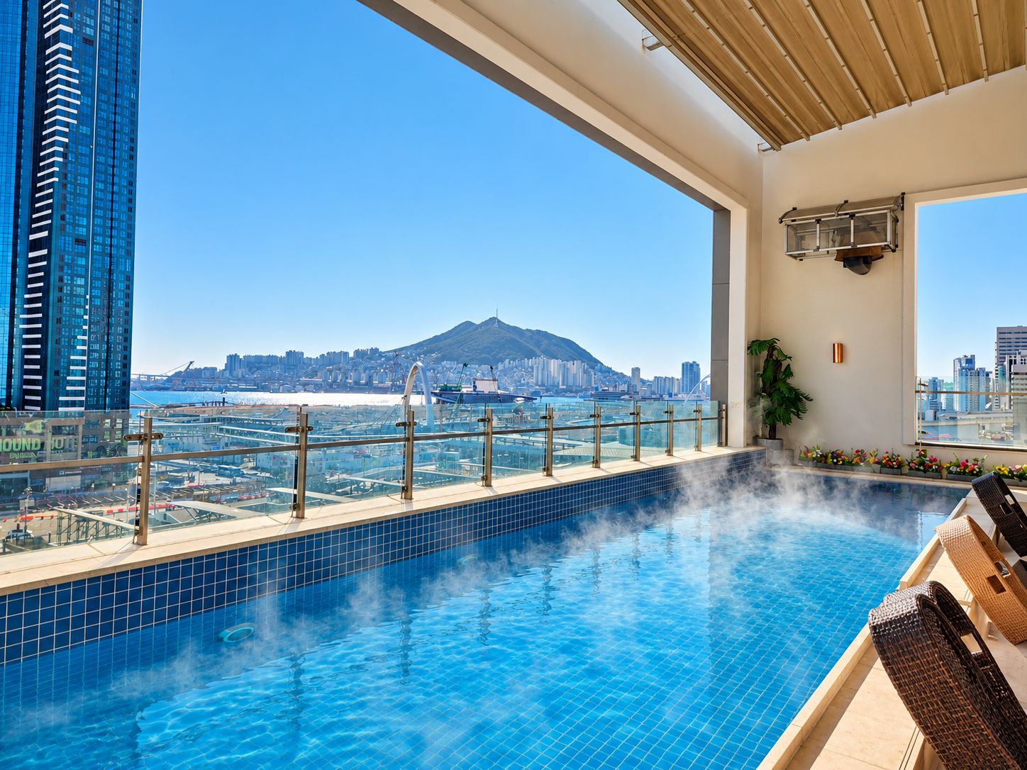 Une piscine sur le toit offrant une vue dégagée sur le paysage urbain et une montagne à l’horizon.
