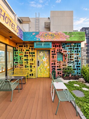 Un hotel con paredes exteriores coloridas, una terraza de madera con asientos al aire libre y una entrada visible.