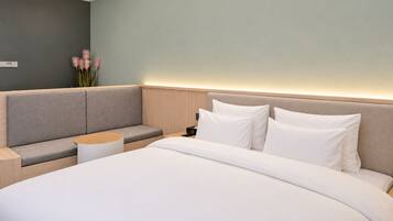 A modern hotel room with a large bed, a seating area, and a nightstand.