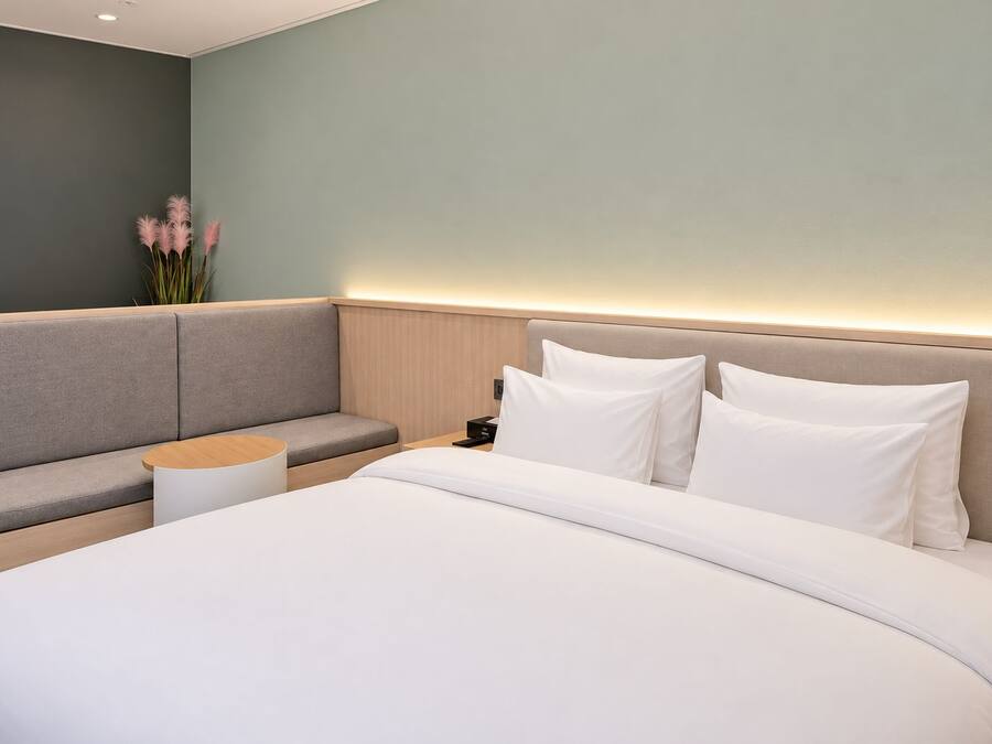 A modern hotel room with a large bed, a seating area, and a nightstand.
