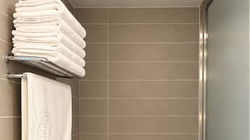 A modern bathroom with a toilet, a towel rack with folded towels, a toilet paper holder, and a trash bin.
