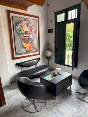 A room with a black leather sofa, a coffee table with a magazine, a framed painting, and a window with a view of greenery.