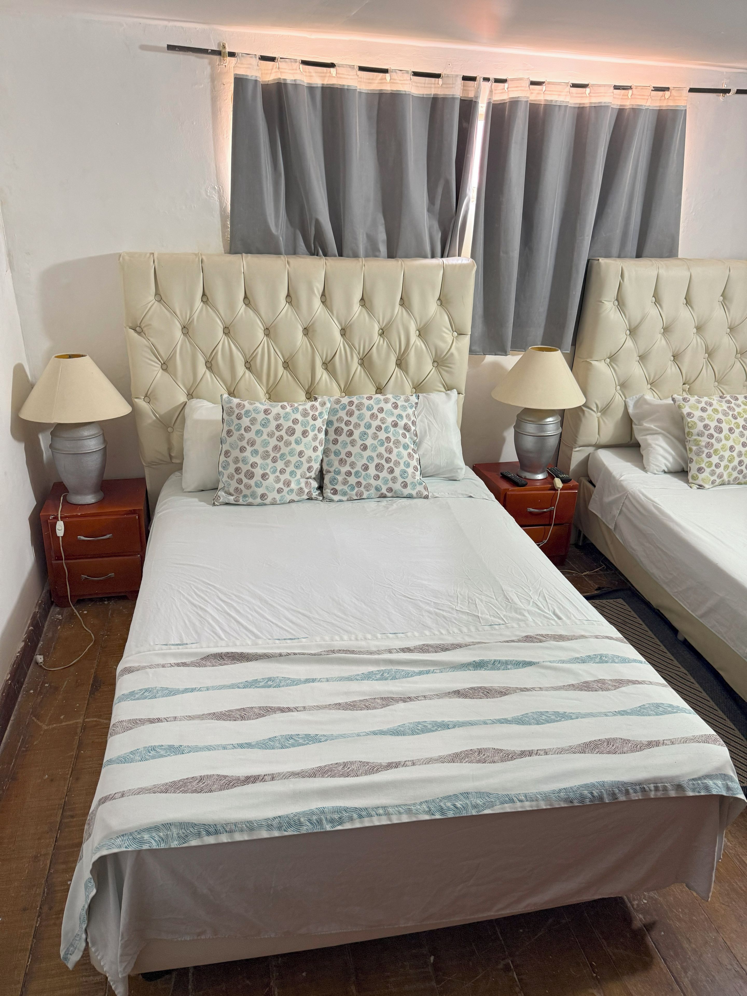 Cama de casal com cabeceira estofada, duas luminárias de cabeceira, almofadas estampadas e colcha listrada.