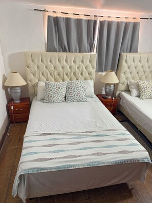 Cama doble con cabecera capitonada, dos lámparas de noche, almohadas estampadas y colcha a rayas.