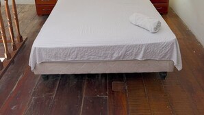 Quarto com cabeceira estofada, duas mesas de cabeceira com luminárias, cama com colcha branca e duas almofadas decorativas.