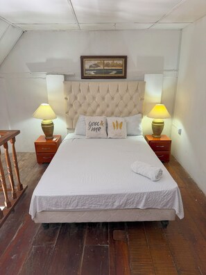Une chambre à coucher avec une tête de lit capitonnée, deux tables de chevet avec des lampes, un lit recouvert d’une courtepointe blanche et deux coussins décoratifs.