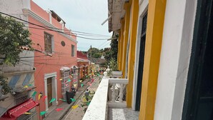 Uma varanda com vista para uma rua repleta de edifícios, alguns com varandas e plantas.