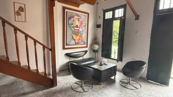 Una habitación con una escalera de madera, un sillón de cuero negro, suelo de baldosas de mármol, un cuadro en la pared y una ventana con vistas.