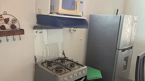 Cozinha compacta com fogão a gás, micro-ondas e geladeira.