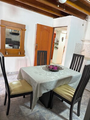 Un coin repas avec une table dressée pour quatre personnes, une porte en bois portant le numéro 202 et un miroir qui reflète la pièce.