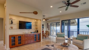 A spacious living area with a large TV, wooden cabinets, and a dining table.