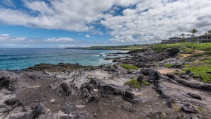 A coastal landscape with rocky terrain, a clear sky, and distant buildings.