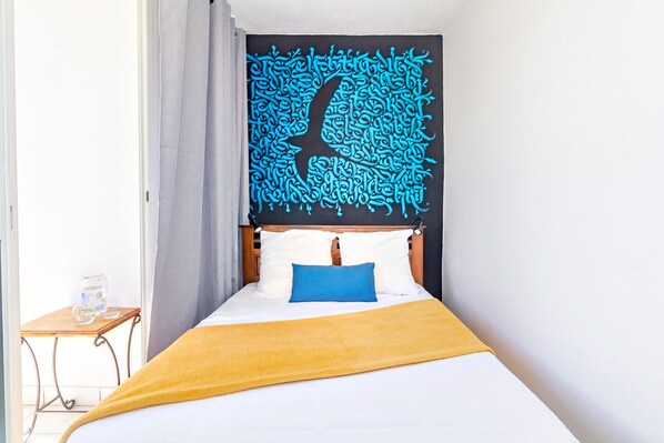 A bedroom with a bed, a wooden headboard, a blue pillow, a yellow blanket, and a wall tapestry.