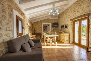 Uma sala de estar aconchegante com sofá, mesa de jantar e cozinha, apresentando paredes de pedra e armários de madeira.
