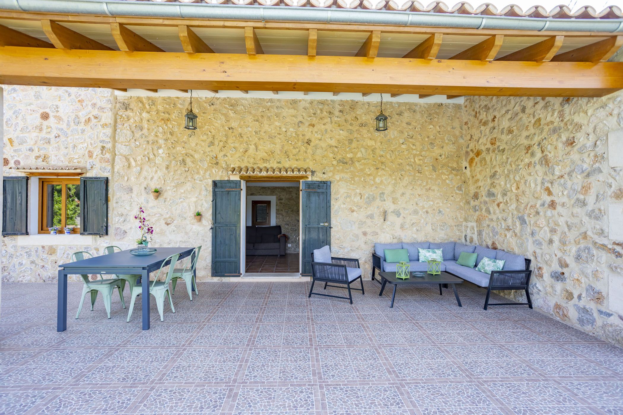 Patio esterno con pareti in pietra, un tavolo e sedie, un divano e lanterne appese.