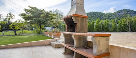 An outdoor barbecue area with a stone chimney, built-in benches, and a paved patio.