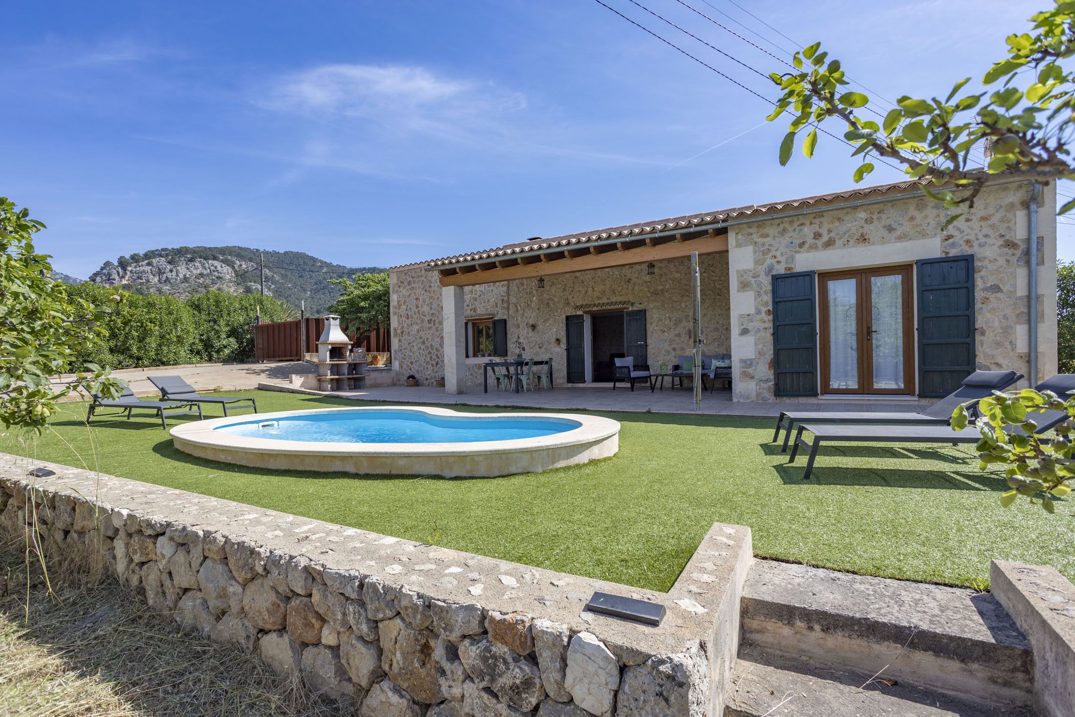 A stone house with a swimming pool, outdoor seating, and a view of the mountains.