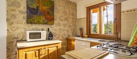 A kitchen with stone walls, a microwave, a gas stove, wooden cabinets, and a window with a view of greenery.