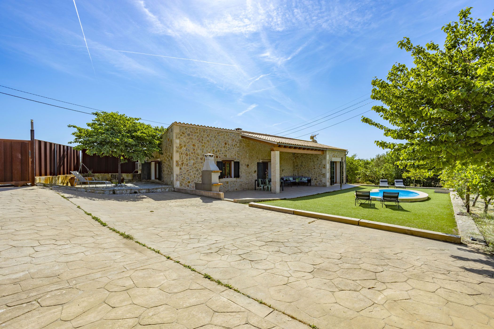 A stone house with a tiled patio, a swimming pool, and a lawn.