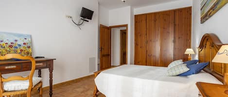 Un dormitorio con una cama de madera, un escritorio con silla, un televisor montado en la pared y un cuadro decorando la pared.