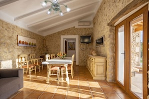 Uma sala de jantar com uma mesa e cadeiras de madeira, um sofá e uma TV fixada na parede.