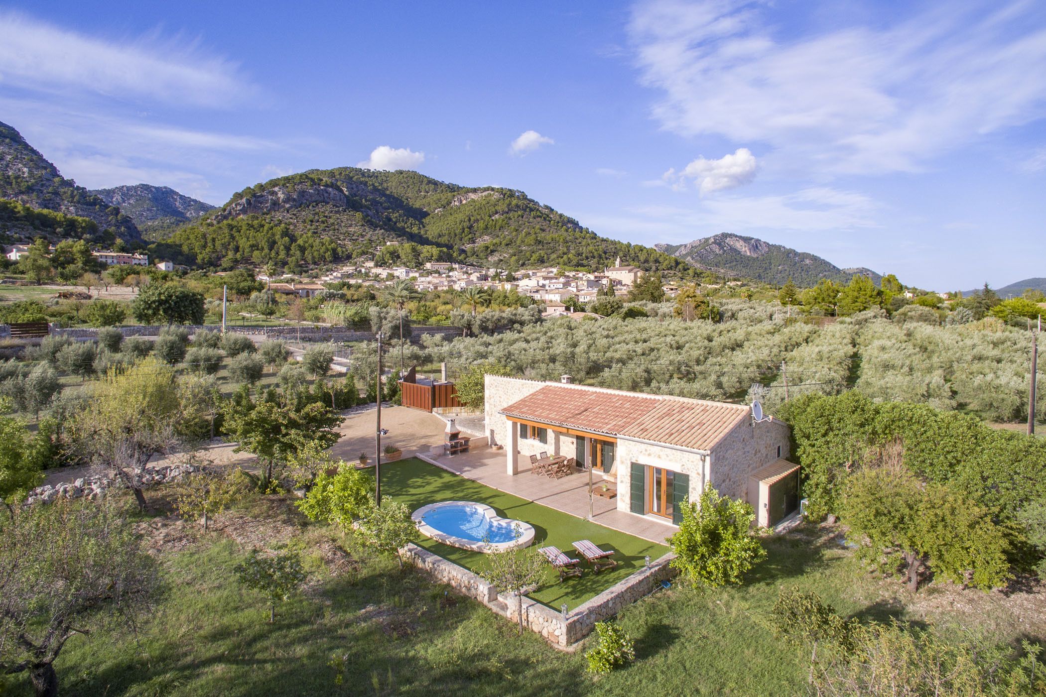 A villa with a swimming pool, outdoor furniture, and a view of the surrounding hills and village.