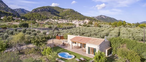 A villa with a swimming pool, outdoor furniture, and a view of the surrounding hills and village.