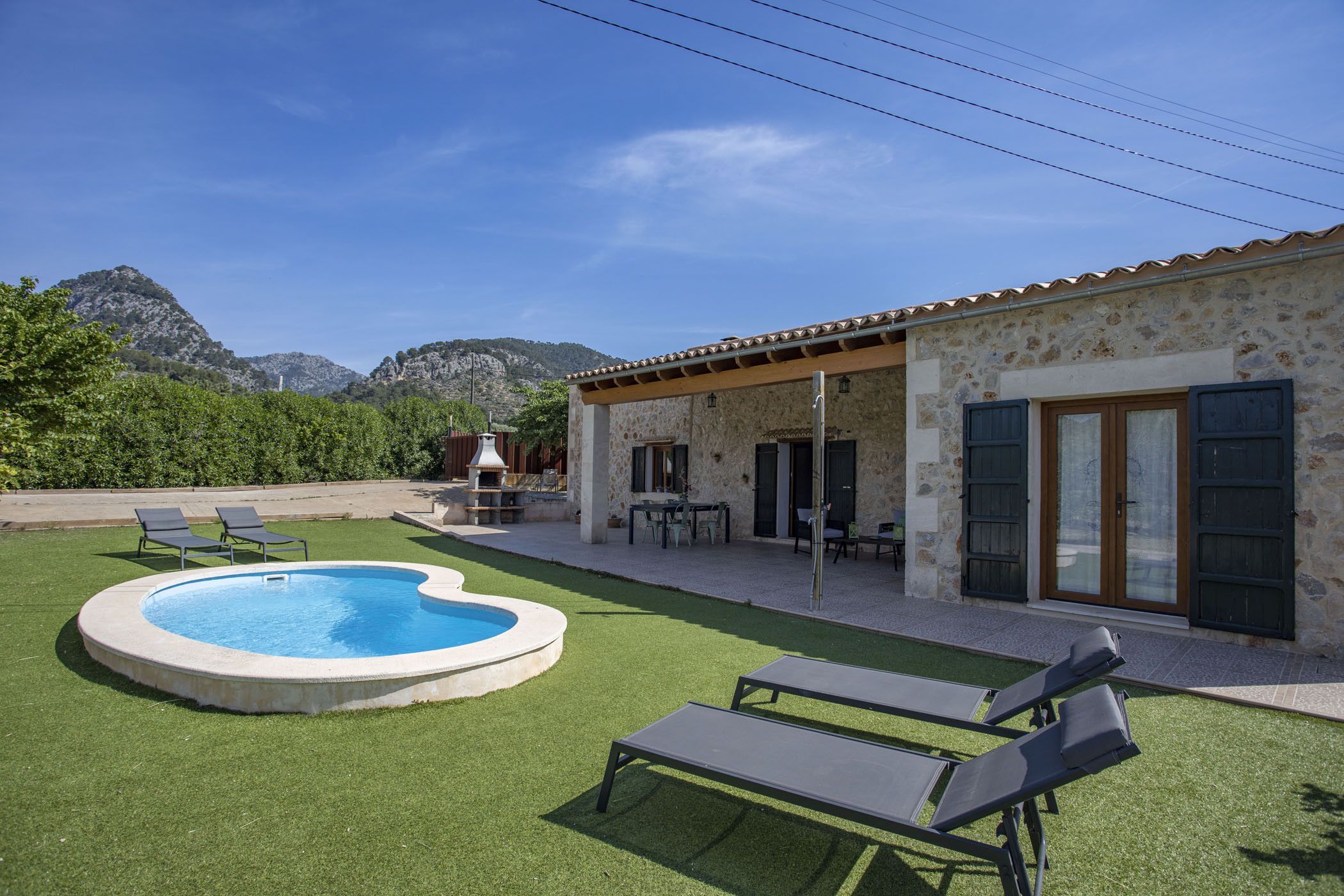 A pool area with a stone building, outdoor furniture, and a mountain backdrop.
