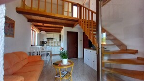 Una sala de estar acogedora con un sofá, una mesita redonda con una planta y una escalera que sube a un nivel superior.