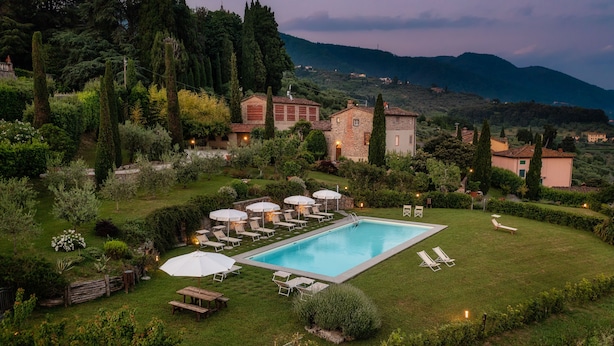 Un espace piscine doté de chaises longues et de parasols, entouré d’une pelouse bien entretenue et, en arrière-plan, d’un bâtiment en pierre.