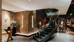 A modern interior with a curved staircase, a reception desk, and a seating area. - DO & CO Hotel München (Munich)