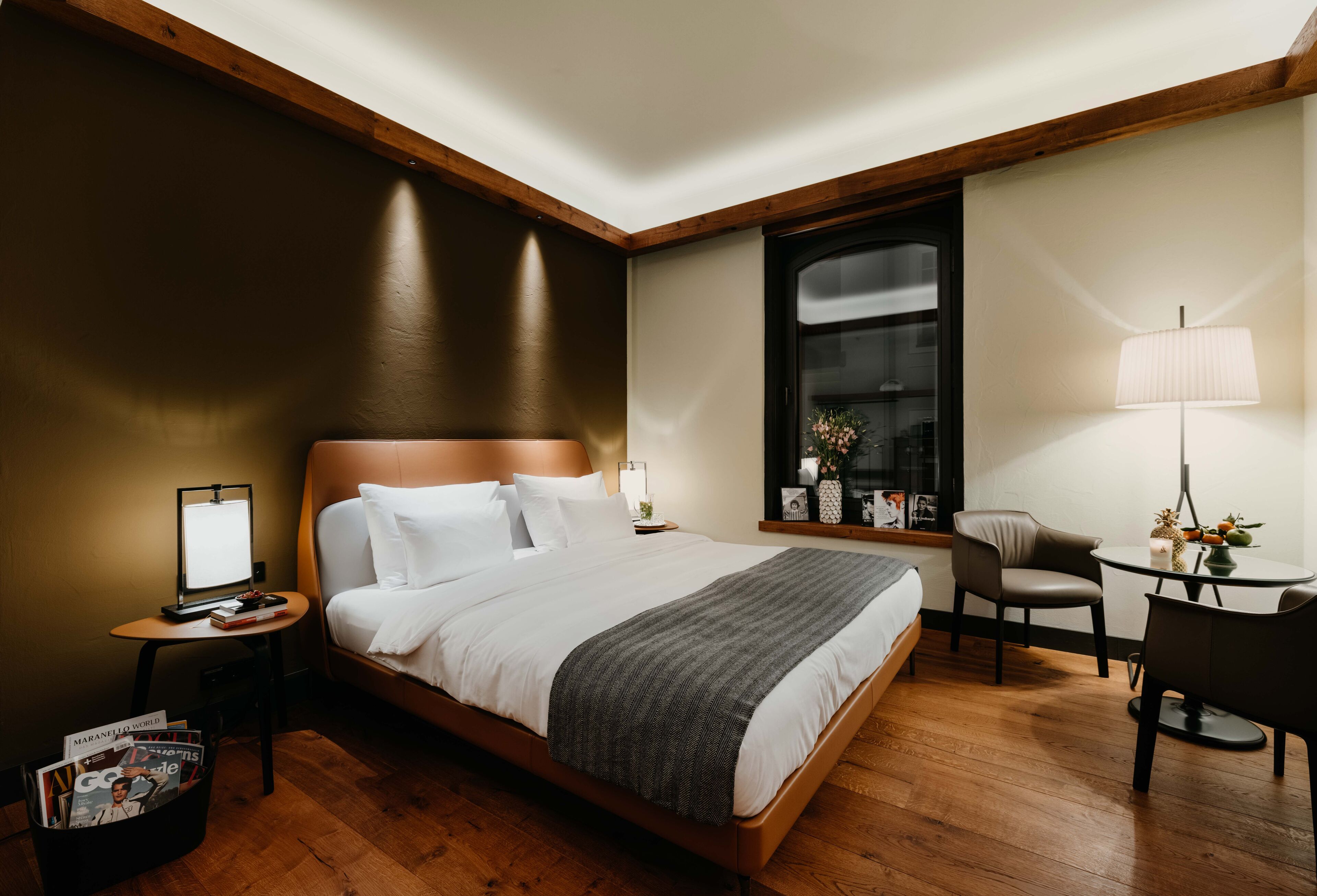Una habitación de hotel con una cama grande, una mesita de noche con lámpara, una pequeña mesa con una silla y una ventana con vistas.