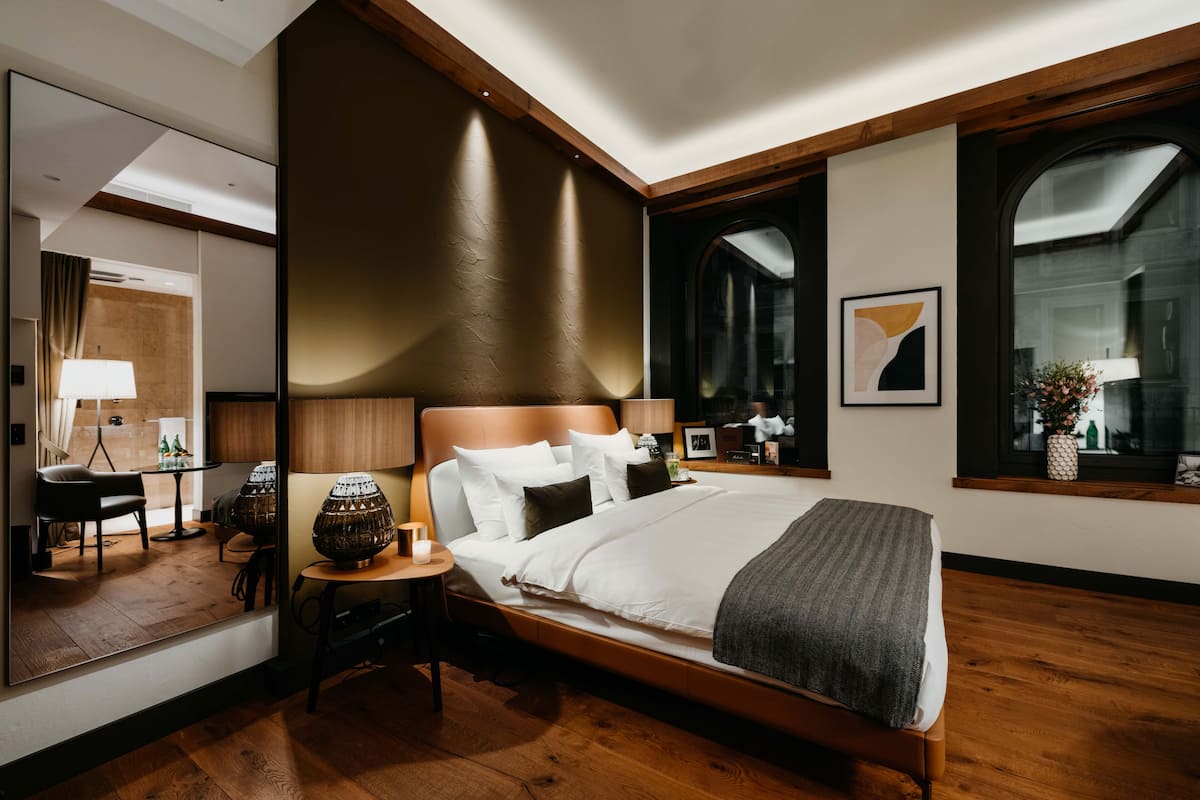 A modern hotel room with a large bed, a wooden headboard, a mirror, and a window with a view.