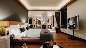 A modern hotel room with a large bed, a TV, and a dining area. - DO & CO Hotel München (Munich)